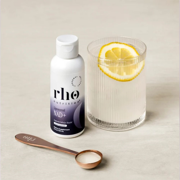 RHO Nutrition Liposomal NAD+ bottle next to a glass of water with a lemon inside.